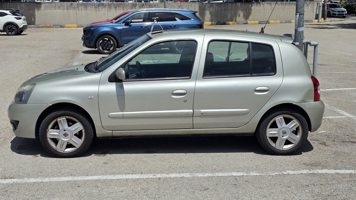 Renault Clio Campus argentée de 2008 de profil gauche en juin 2026, avec un choc sur la porte arrière et la moulure tordue